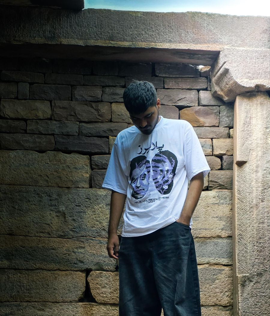 Person wearing a white t-shirt with graphic design standing against a stone wall.